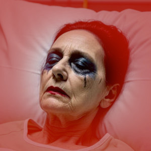 A close view of an unwell woman in a hospital bed, she wears smeared lipstick and mascara that has run.